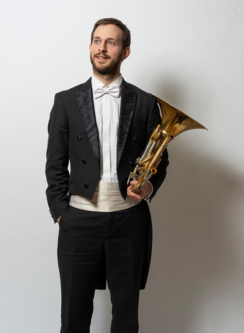 Hornist Pascal Deuber mit Horn im Anzug vor weißem Hintergrund
